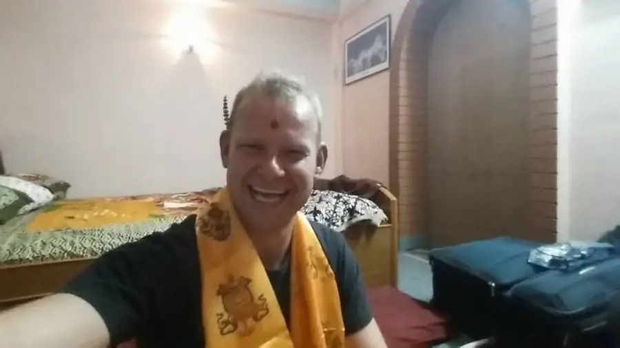 A laughing selfie wearing a yellow blessing scarf and a red tika on my forehead
