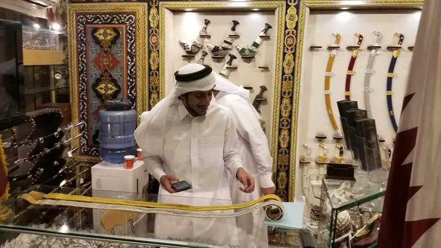 The inside of a shop in Doha with ornate gold and blue painted panels, daggers and curved swords on the wall, and a shopkeeper in white