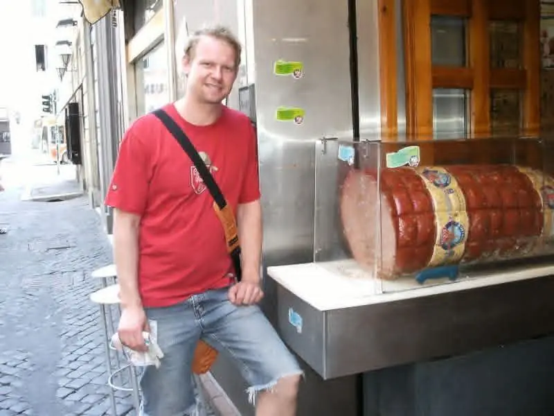 Me next to a shop window with a gigantic mortadella sausage on display